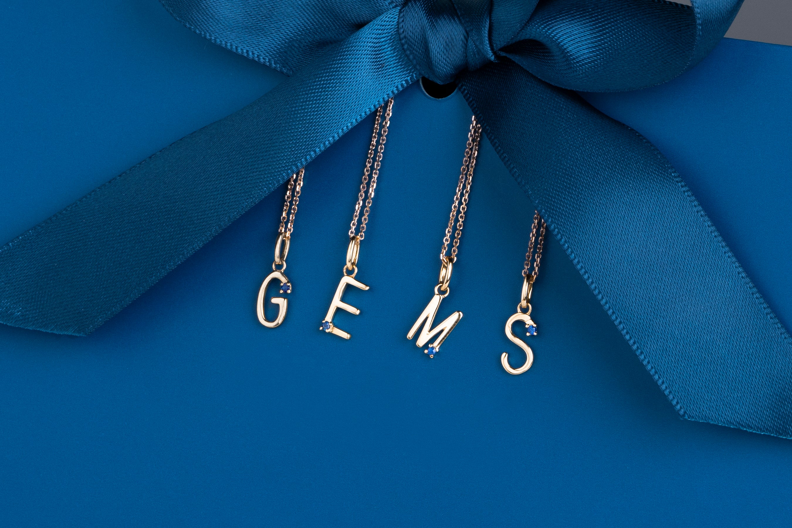 Three gold necklaces with 'GEMS' on a blue background