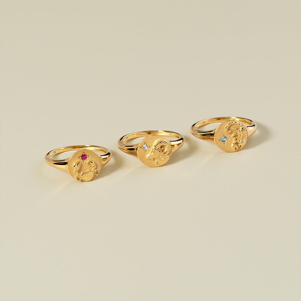 Three gold rings with face designs on a beige background