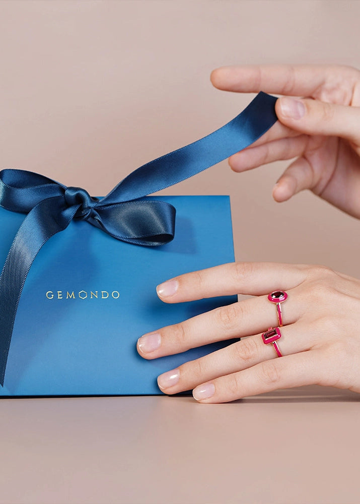Hand with a red ring holding a blue gift box with a bow, featuring the brand 'GEMONDO'.